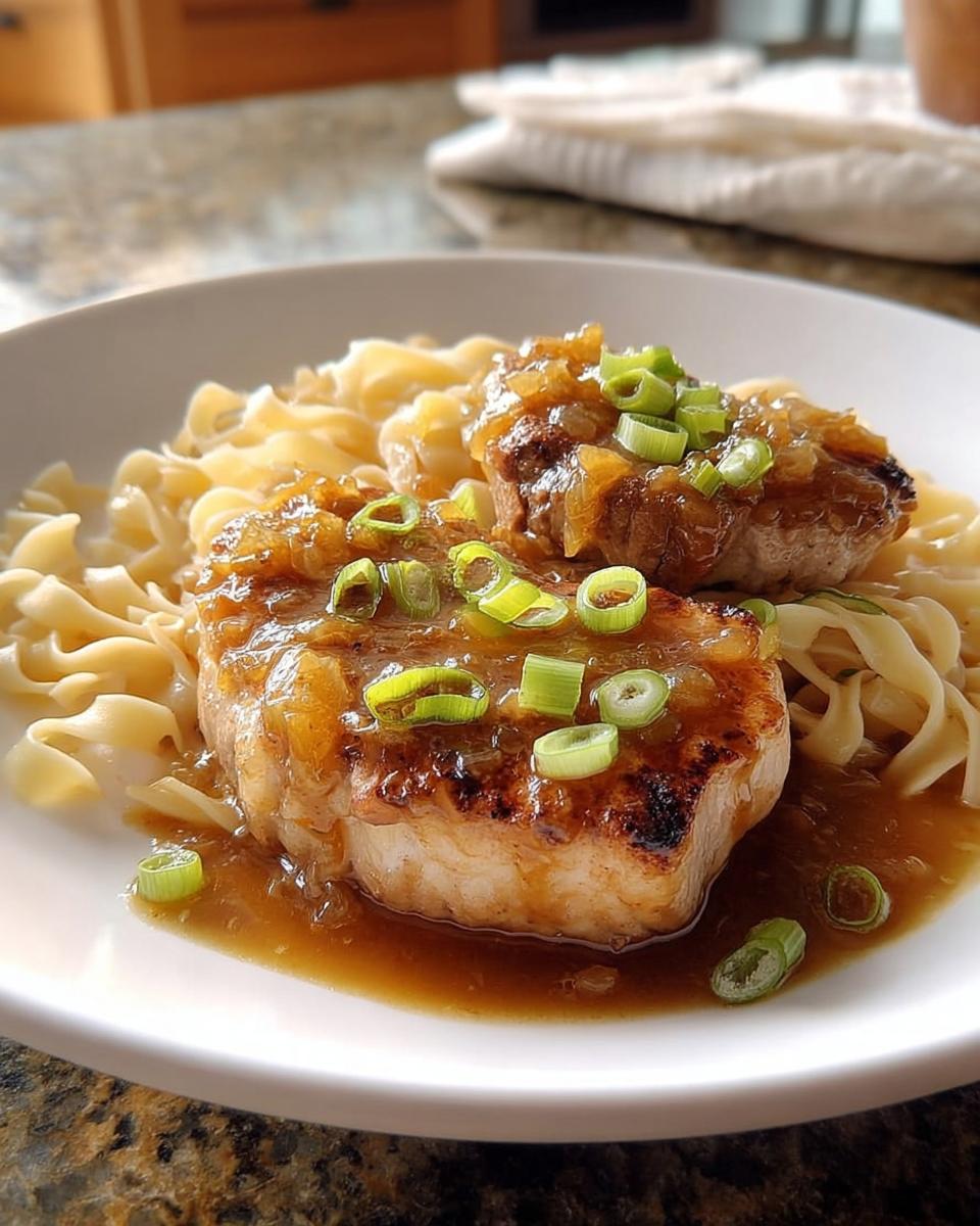 Two juicy 10-ingredient pork chops served over wide egg noodles with a rich gravy and garnished with chopped green onions.