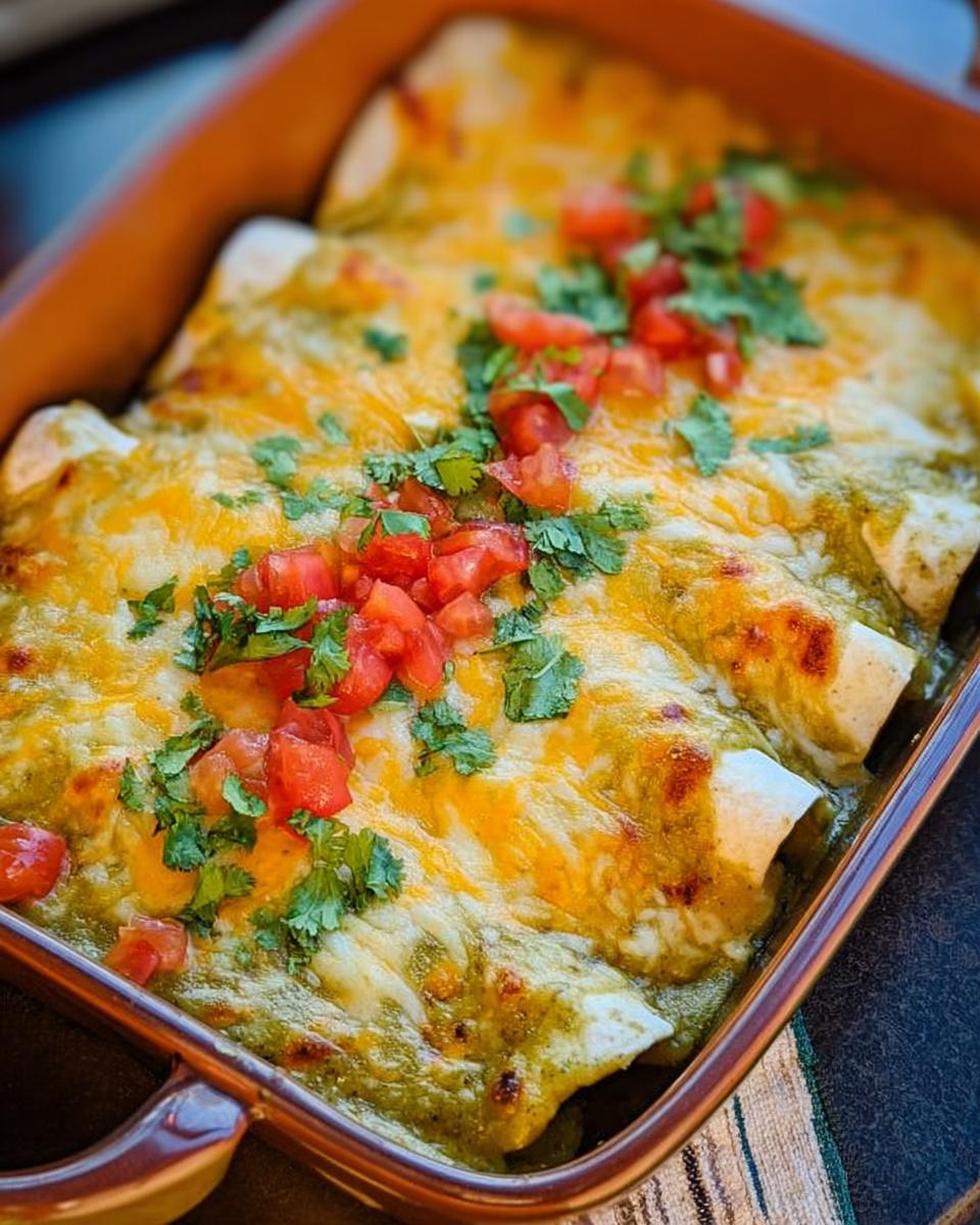 Close-up of baked chicken enchiladas topped with melted cheese, salsa verde, diced tomatoes, and cilantro.