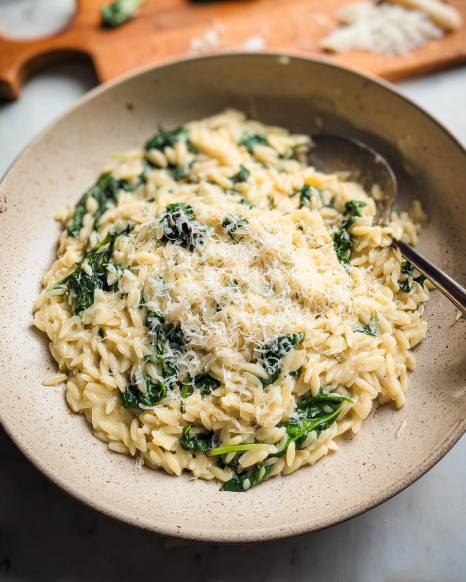 A close-up of creamy spinach orzo topped with grated parmesan cheese, a delicious veggie side dish.