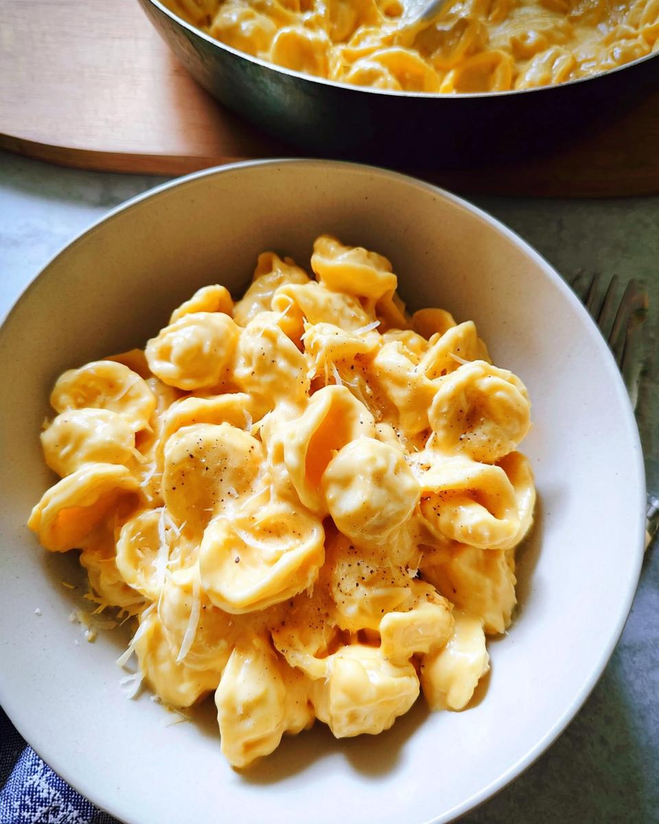 A bowl of creamy orecchiette pasta with cheese sauce, sprinkled with pepper and Parmesan, perfect for easy dinner recipes.
