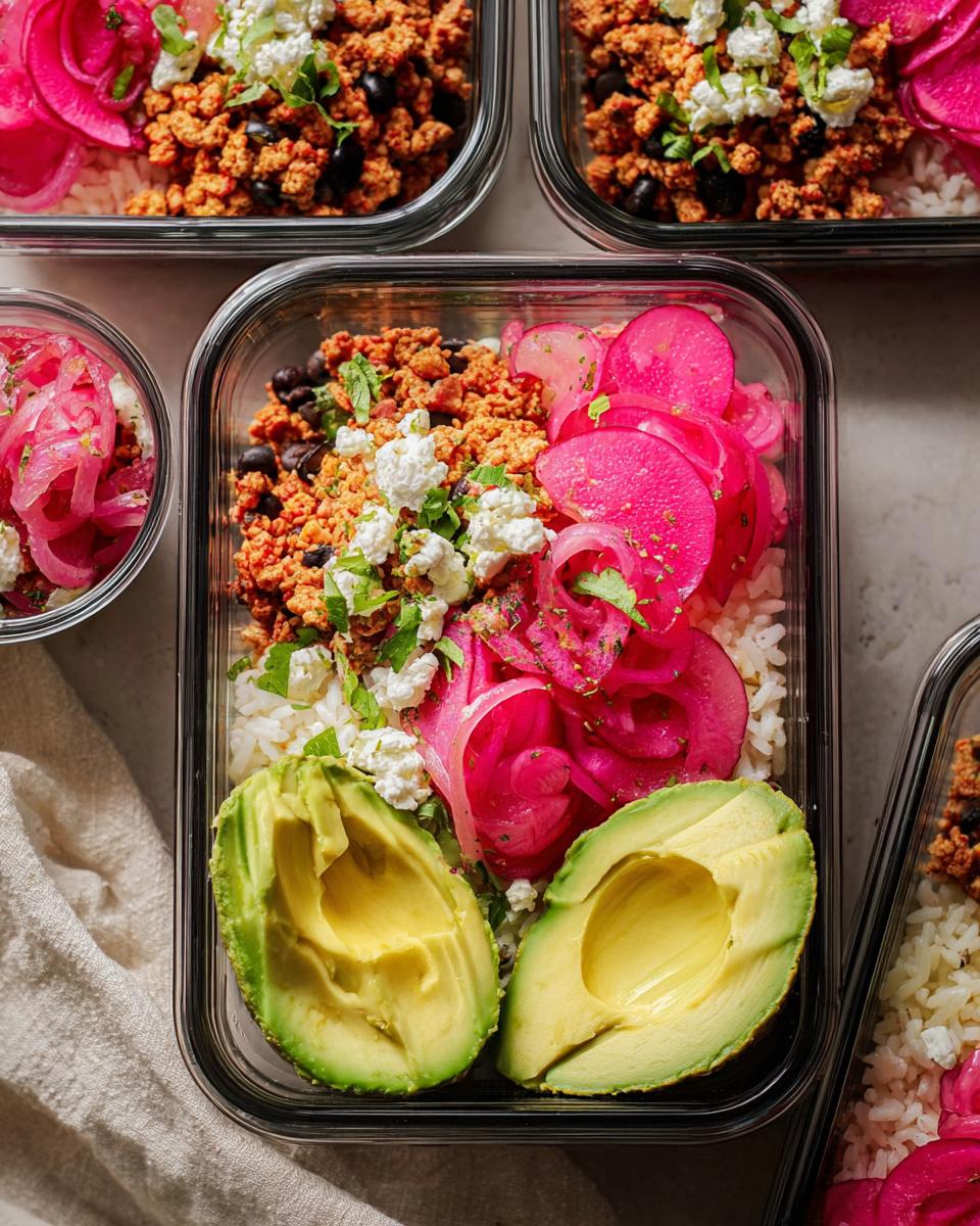 Overhead view of meal prep containers filled with rice bowls, featuring seasoned ground meat, black beans, pickled red onions, avocado halves, and crumbled cheese.