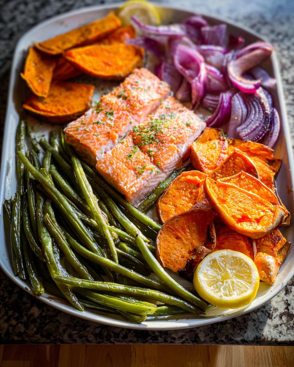 Sheet pan of salmon recipes meal prep with roasted sweet potatoes, green beans, red onion, and lemon.