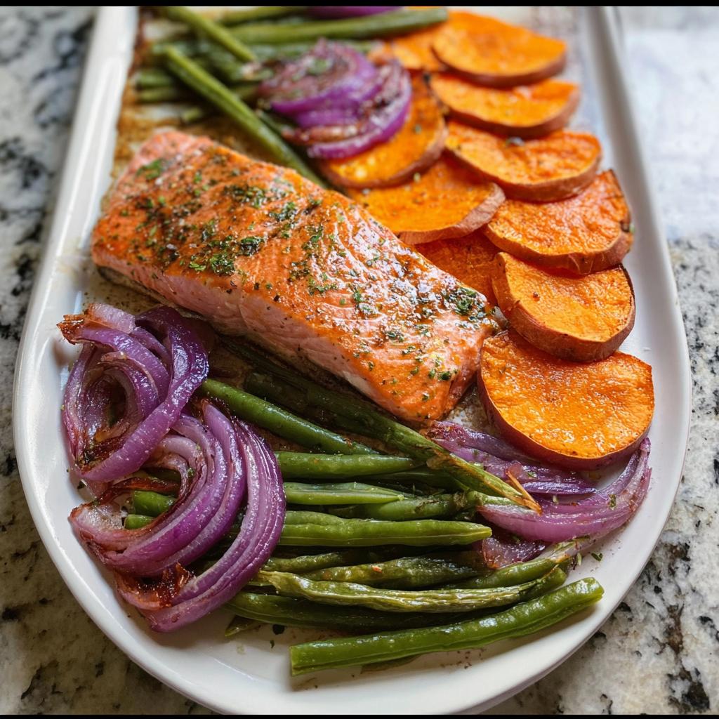 A delicious sheet pan meal prep featuring a salmon fillet, roasted sweet potato slices, green beans, and red onion.
