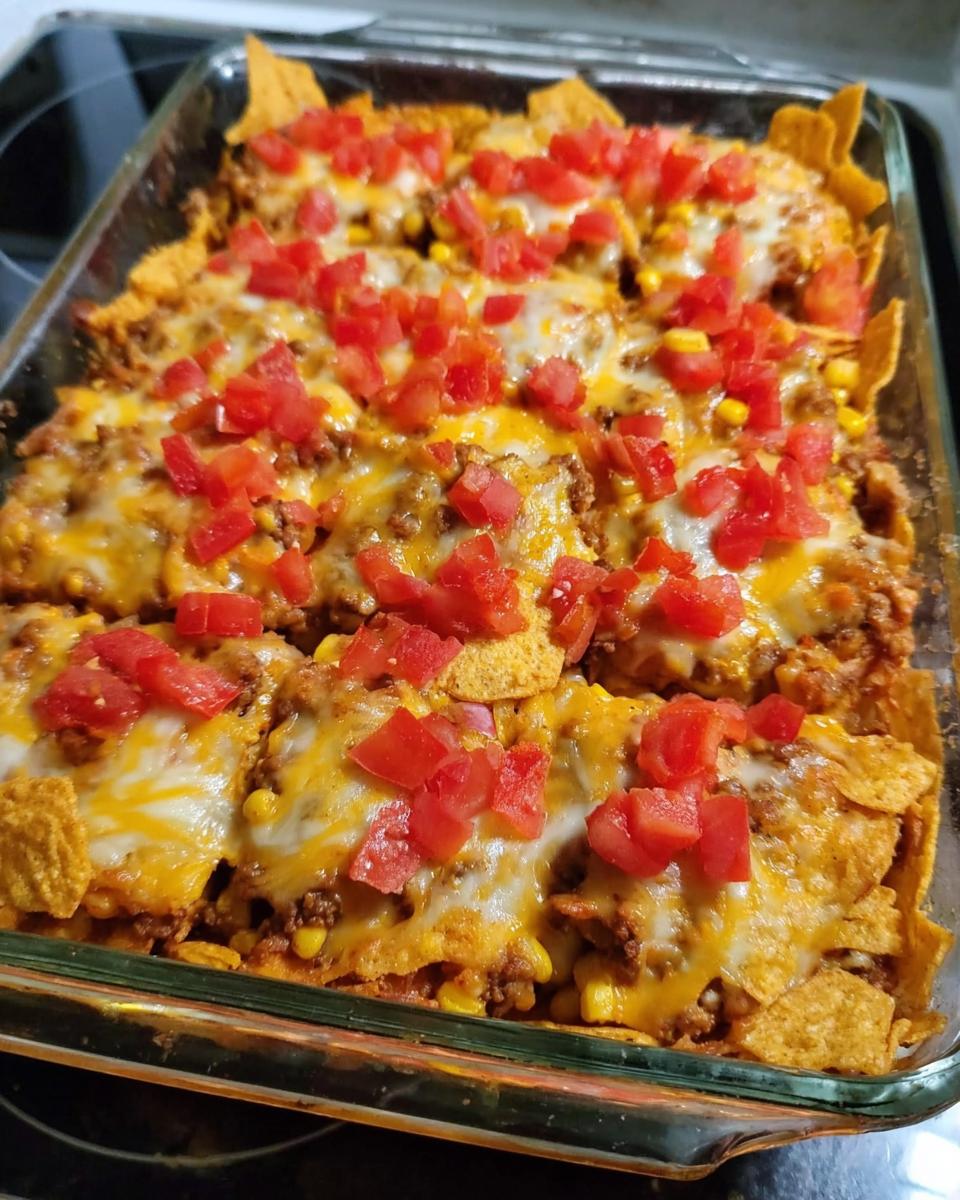 A close-up of a baked Taco Tuesday recipe casserole in a glass dish, topped with melted cheese, corn, and diced tomatoes.
