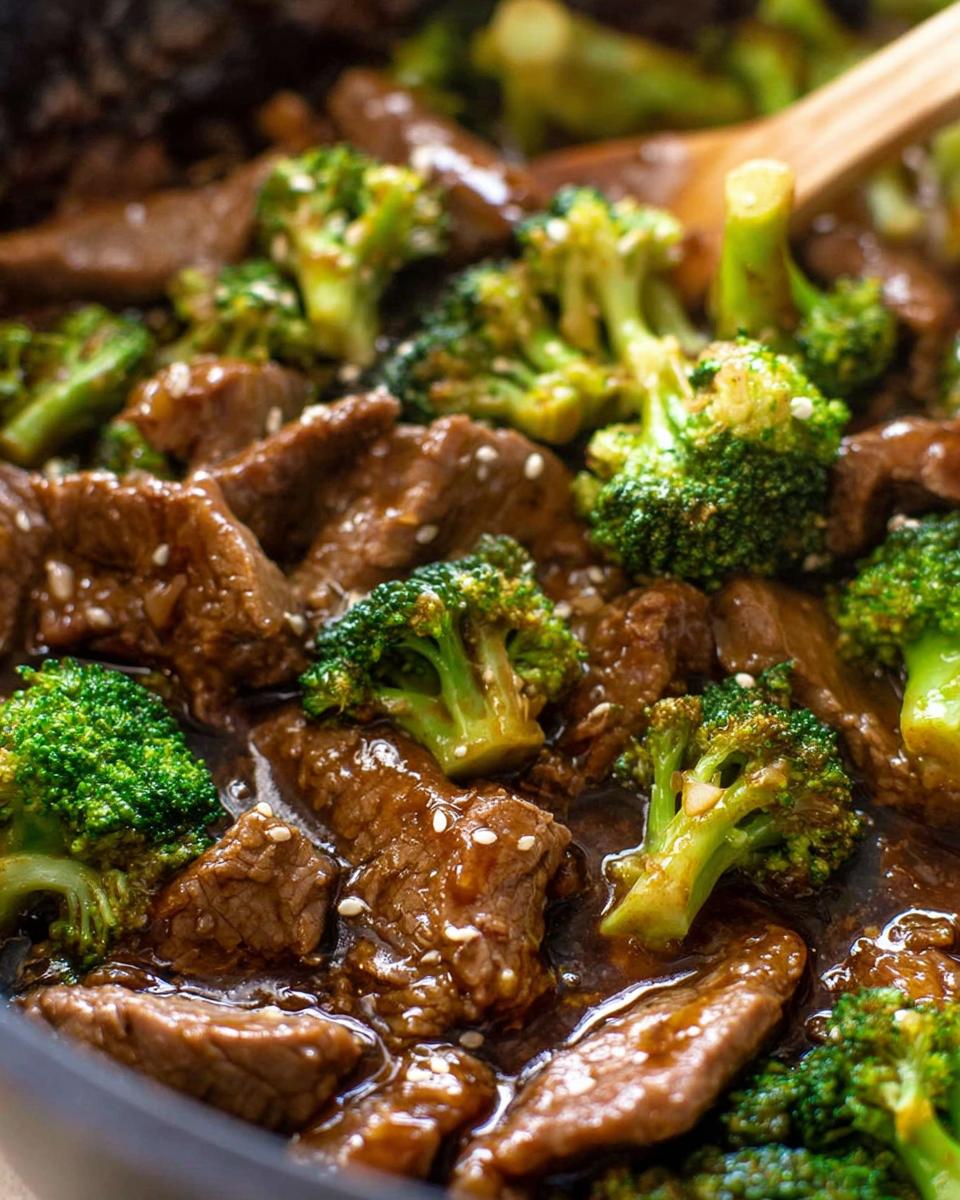 Close-up of tender slices of Chinese Beef and Broccoli coated in a glossy sauce, sprinkled with sesame seeds.