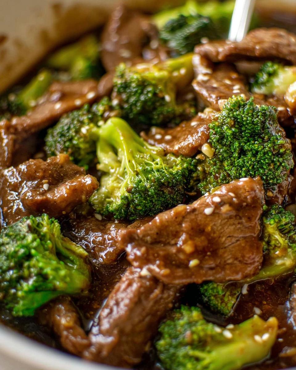 Close-up of tender slices of beef and vibrant broccoli florets coated in a glossy sauce, sprinkled with sesame seeds.