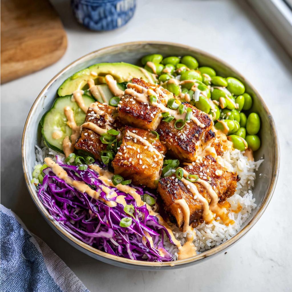 A delicious Crispy Salmon and Rice Bowl with avocado, cucumber, edamame, and shredded red cabbage, drizzled with sauce.