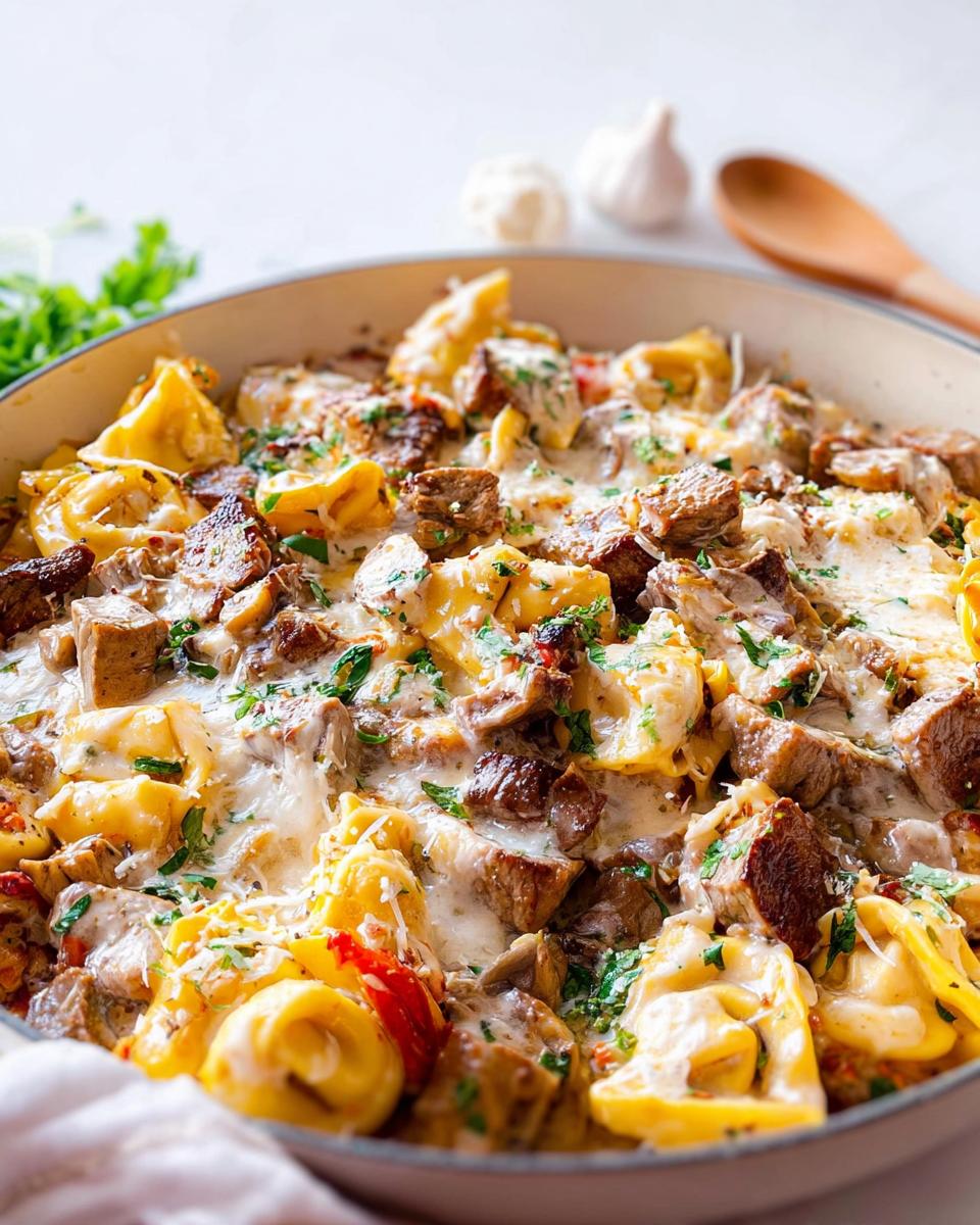 A close-up of a skillet filled with Garlic Steak Tortellini, featuring pasta, tender steak pieces, and melted cheese.