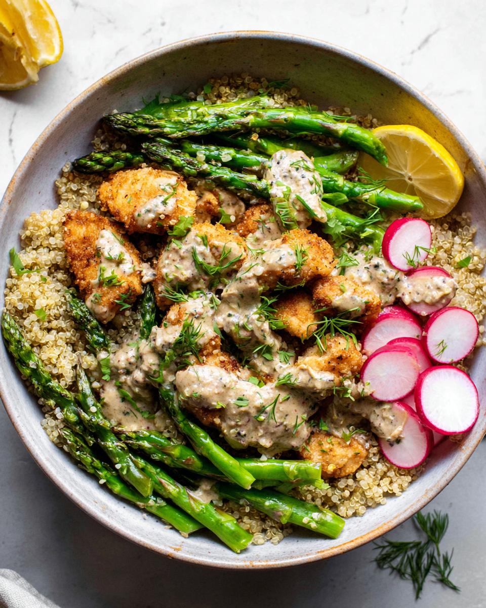 A healthy lemon garlic chicken meal prep bowl with quinoa, asparagus, radishes, and creamy sauce.