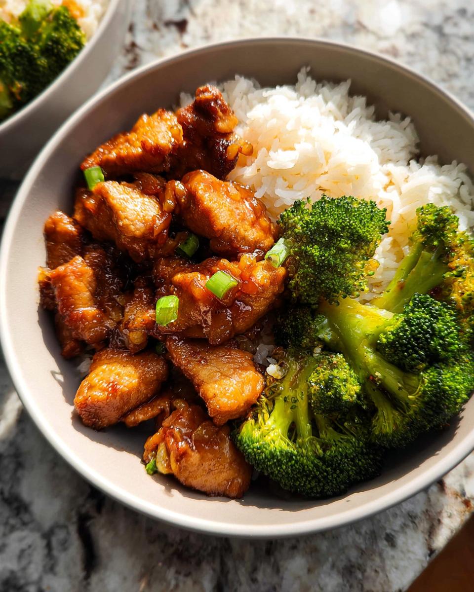 A delicious Honey Garlic Pork Rice Bowl featuring tender pork pieces, fluffy white rice, and vibrant steamed broccoli, garnished with green onions.