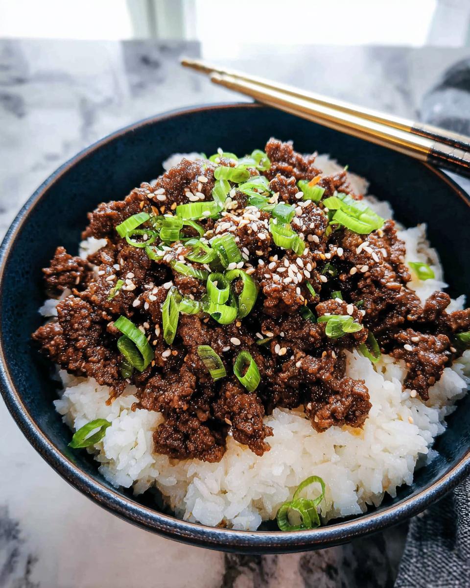 A close-up of a Korean Ground Beef Bowl, featuring seasoned ground beef over white rice, garnished with green onions and sesame seeds.
