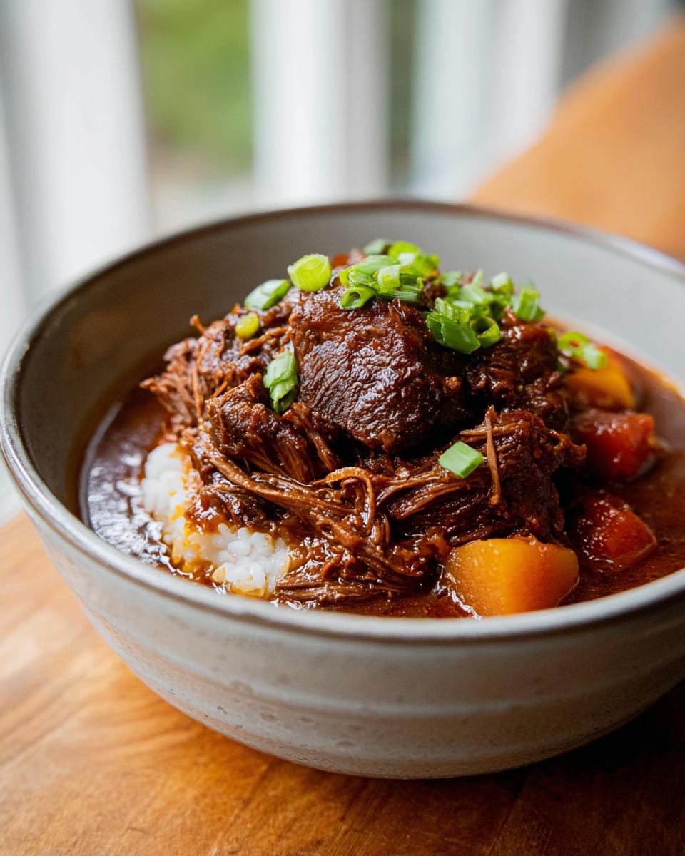 A close-up of a bowl filled with fluffy white rice, topped with shredded Korean Style Pot Roast and garnished with green onions.
