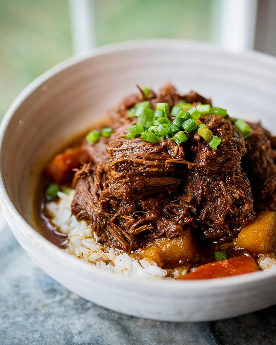 A bowl of fluffy white rice topped with shredded Korean Style Pot Roast and garnished with chopped green onions.
