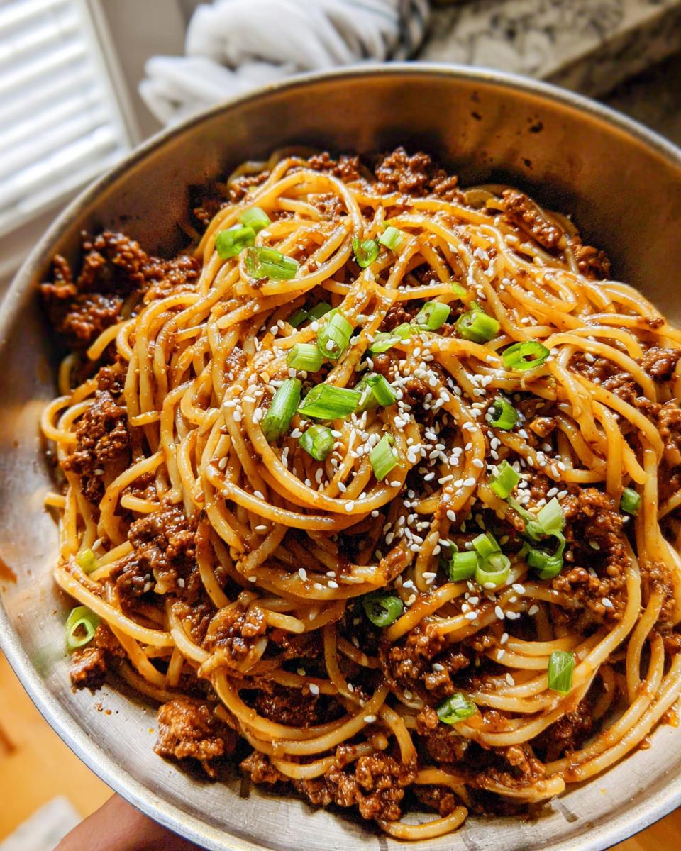 A close-up view of a bowl filled with Mongolian Ground Beef Noodles, garnished with green onions and sesame seeds.
