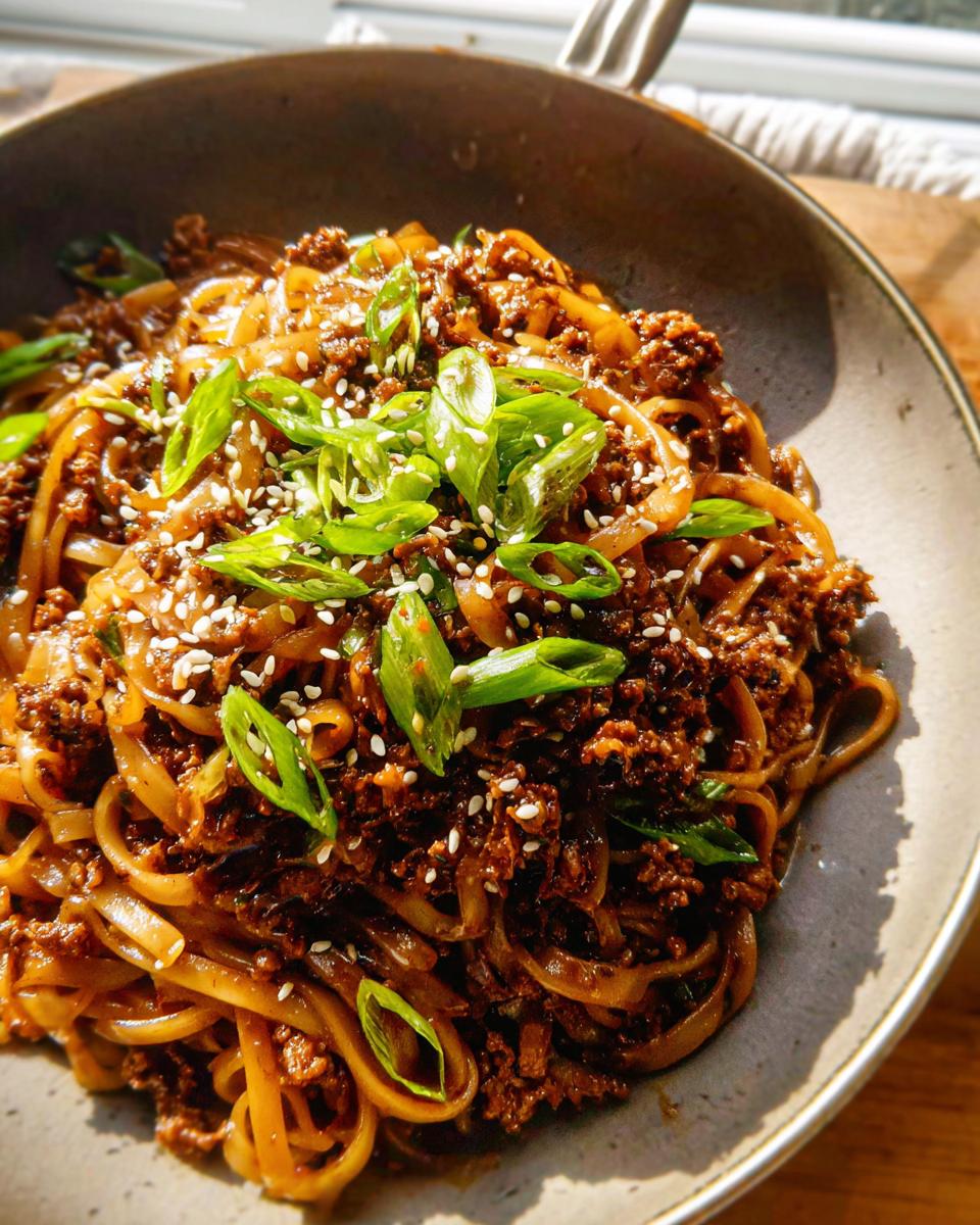 A close-up of a bowl filled with Mongolian Ground Beef Noodles, garnished with green onions and sesame seeds.