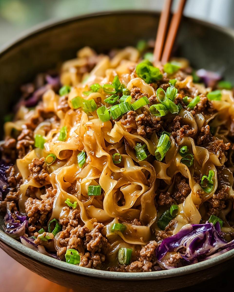 A close-up of a delicious Potsticker Noodle Bowl with Pork & Cabbage Slaw, featuring noodles, ground pork, and green onions.