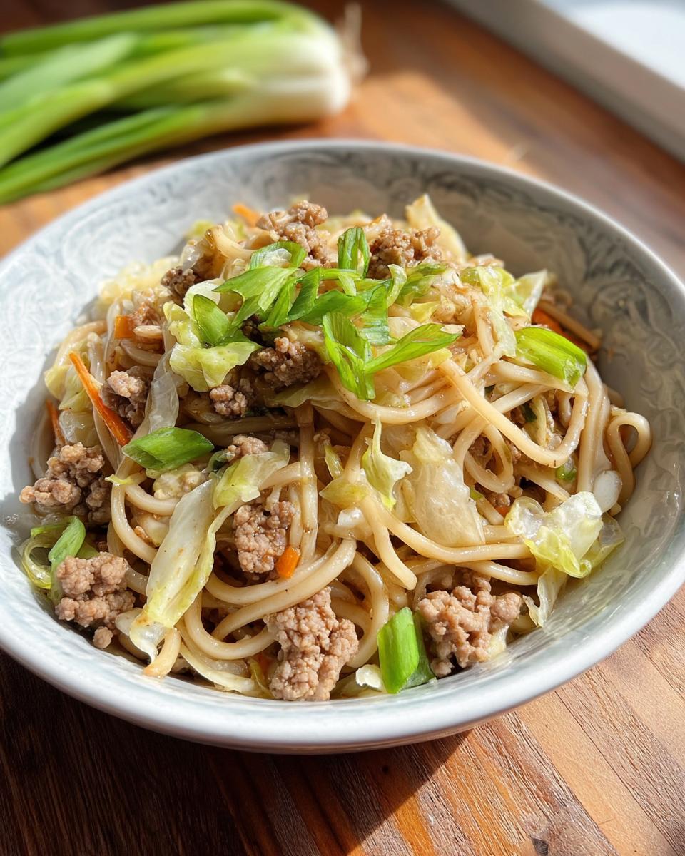 A bowl of Potsticker Noodle Bowl with Pork & Cabbage Slaw, featuring noodles, ground pork, cabbage, and green onions.