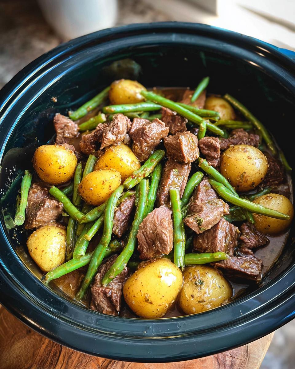 Overhead view of a slow cooker filled with tender chunks of garlic butter beef, whole baby potatoes, and bright green beans.