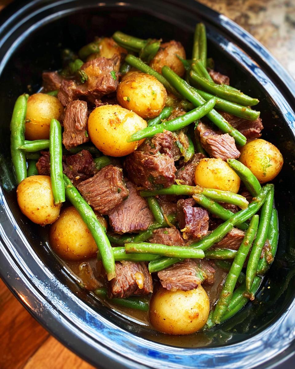 Close-up of tender beef chunks, small potatoes, and green beans in a slow cooker, showcasing the Slow Cooker Garlic Butter Beef with Potatoes.