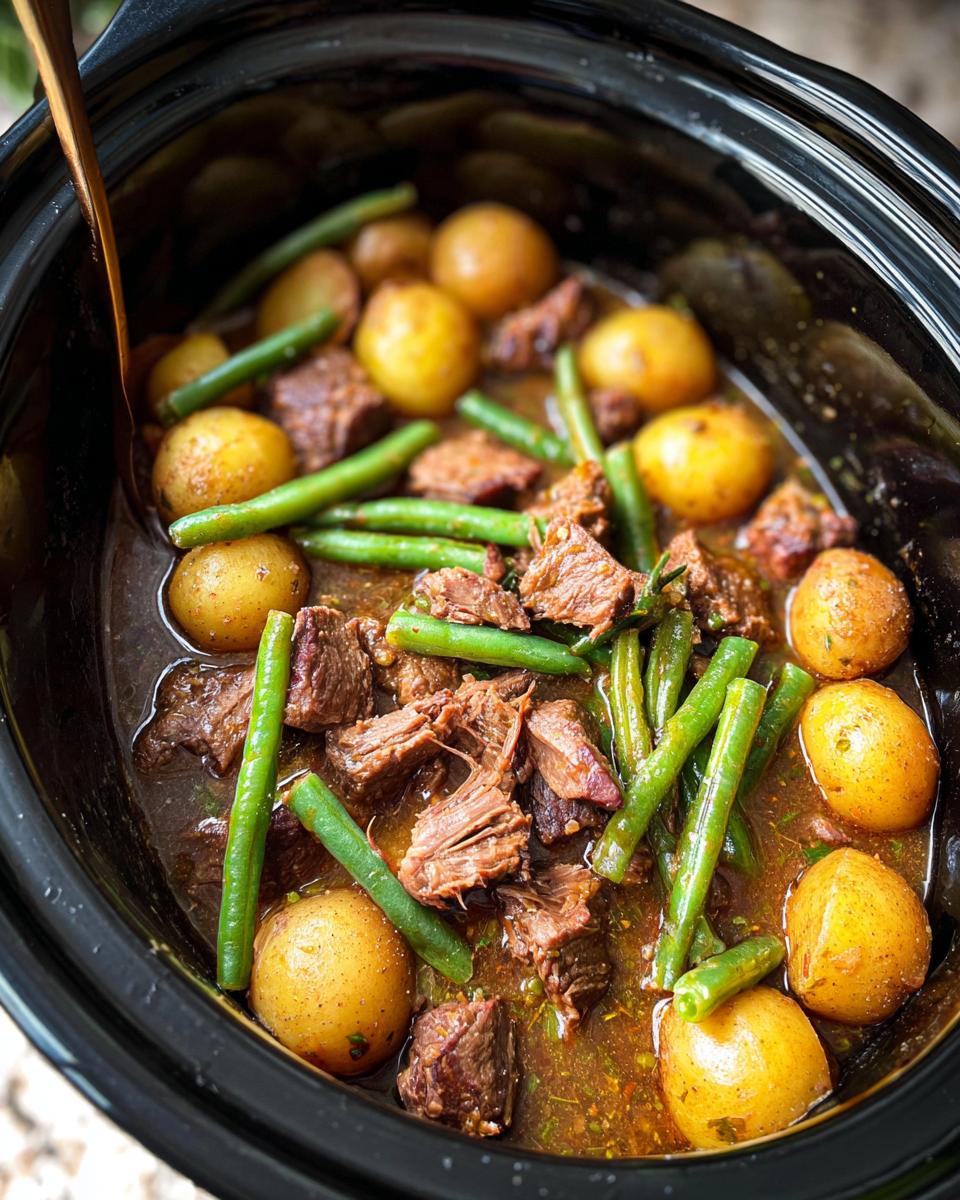 Close-up of Slow Cooker Garlic Butter Beef with Potatoes and Green Beans in a black slow cooker.