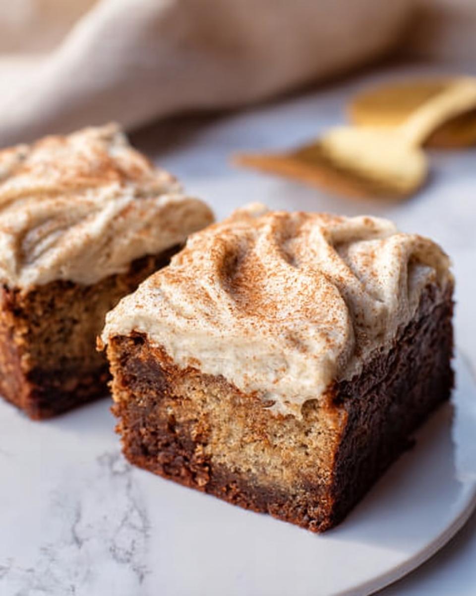 Two slices of Banana Bread Brownies Made Easy, topped with swirled cream cheese frosting and a dusting of cinnamon.
