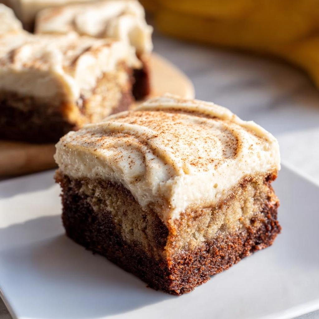 A close-up of a moist Banana Bread Brownie Made Easy, topped with swirled cream cheese frosting and a sprinkle of cinnamon.