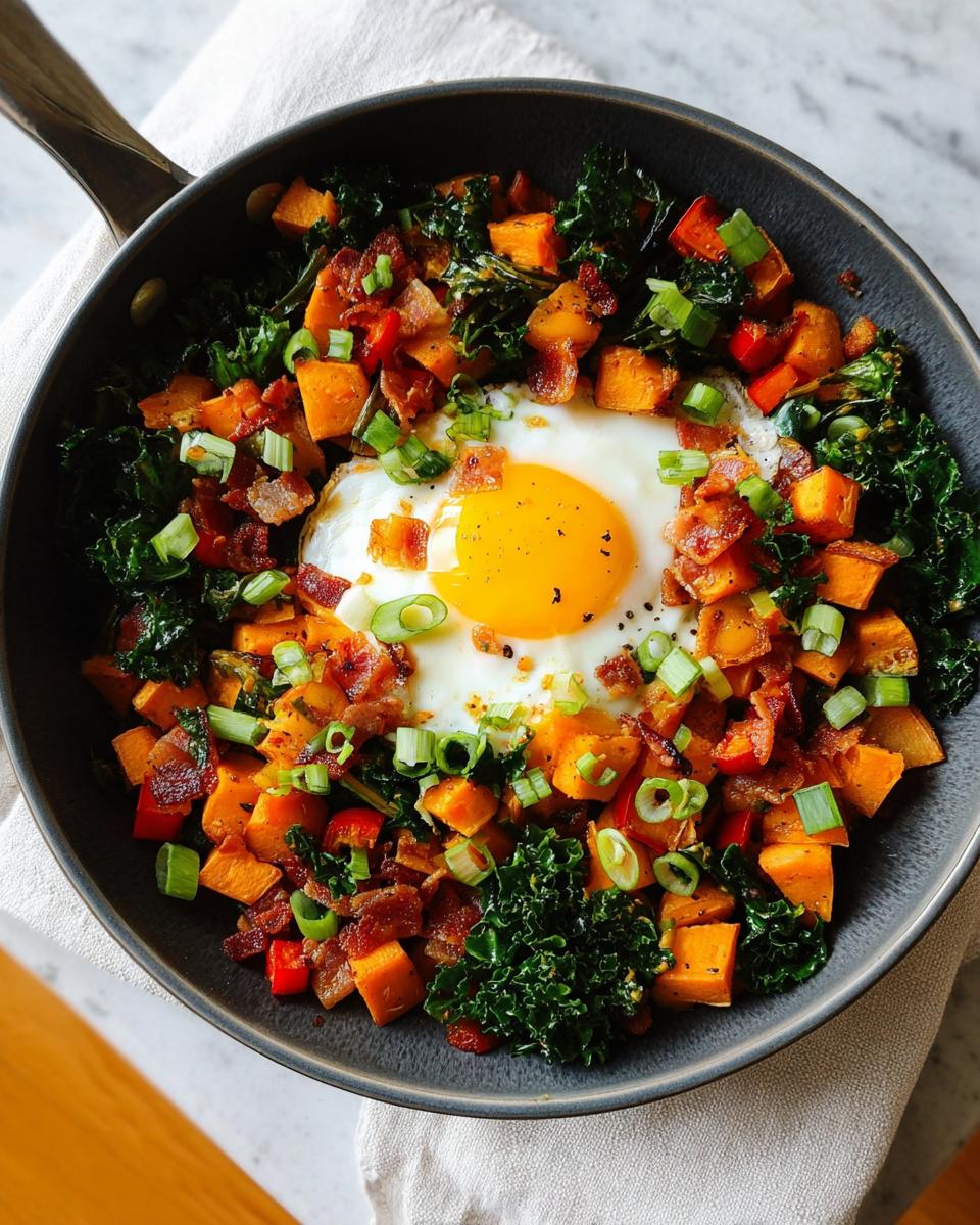 A delicious BREAKFAST SWEET POTATO hash served in a skillet, topped with a fried egg, bacon, and green onions.