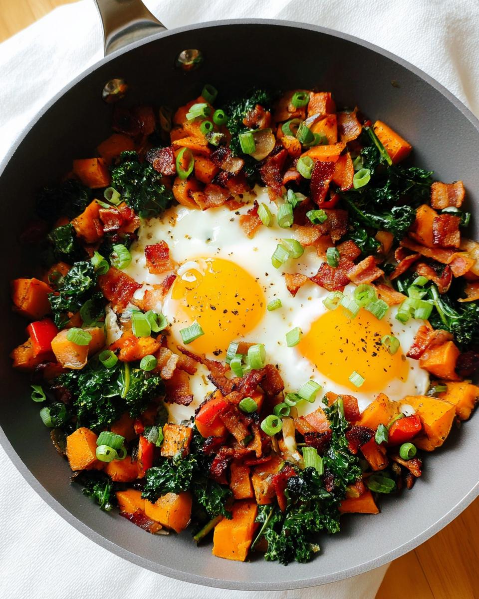 A hearty BREAKFAST SWEET POTATO hash with two fried eggs, crispy bacon, kale, and green onions in a skillet.