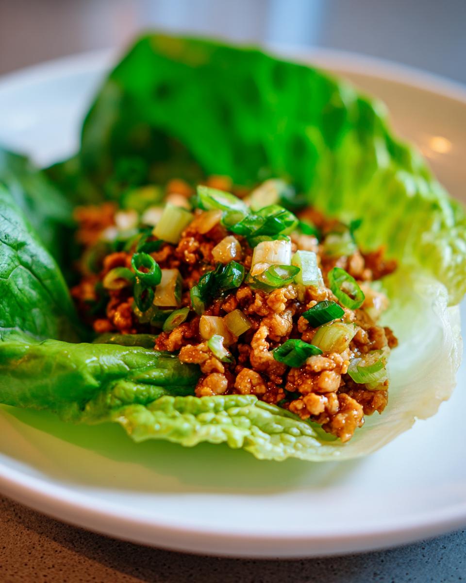 Close-up of a chicken lettuce wrap filled with seasoned ground chicken and topped with green onions.