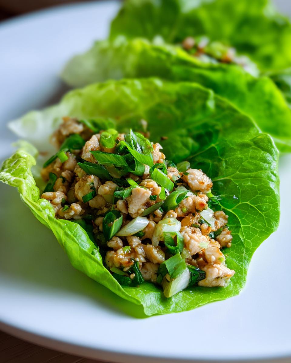 Close-up of a fresh chicken lettuce wrap filled with seasoned ground chicken and green onions.