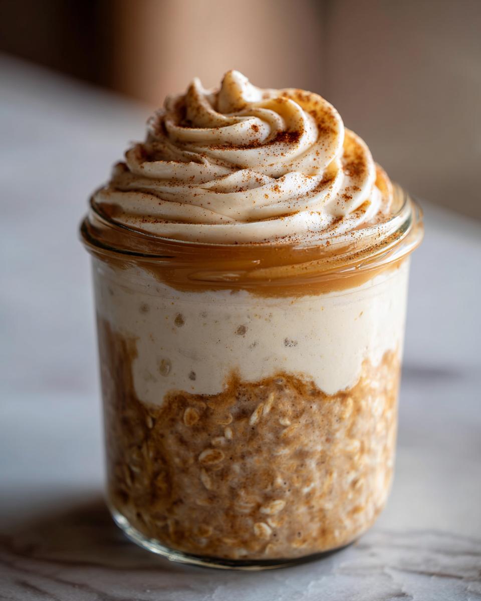 Close-up of cinnamon roll overnight oats in a jar, topped with whipped cream and cinnamon.