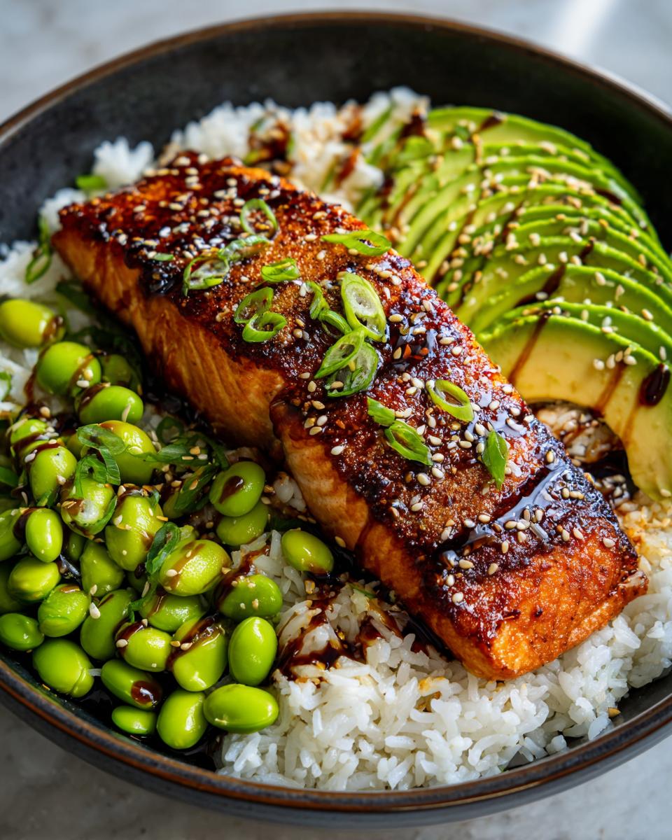 A close-up of a Crispy Salmon and Rice Bowl featuring a glazed salmon fillet, sliced avocado, edamame, and white rice.
