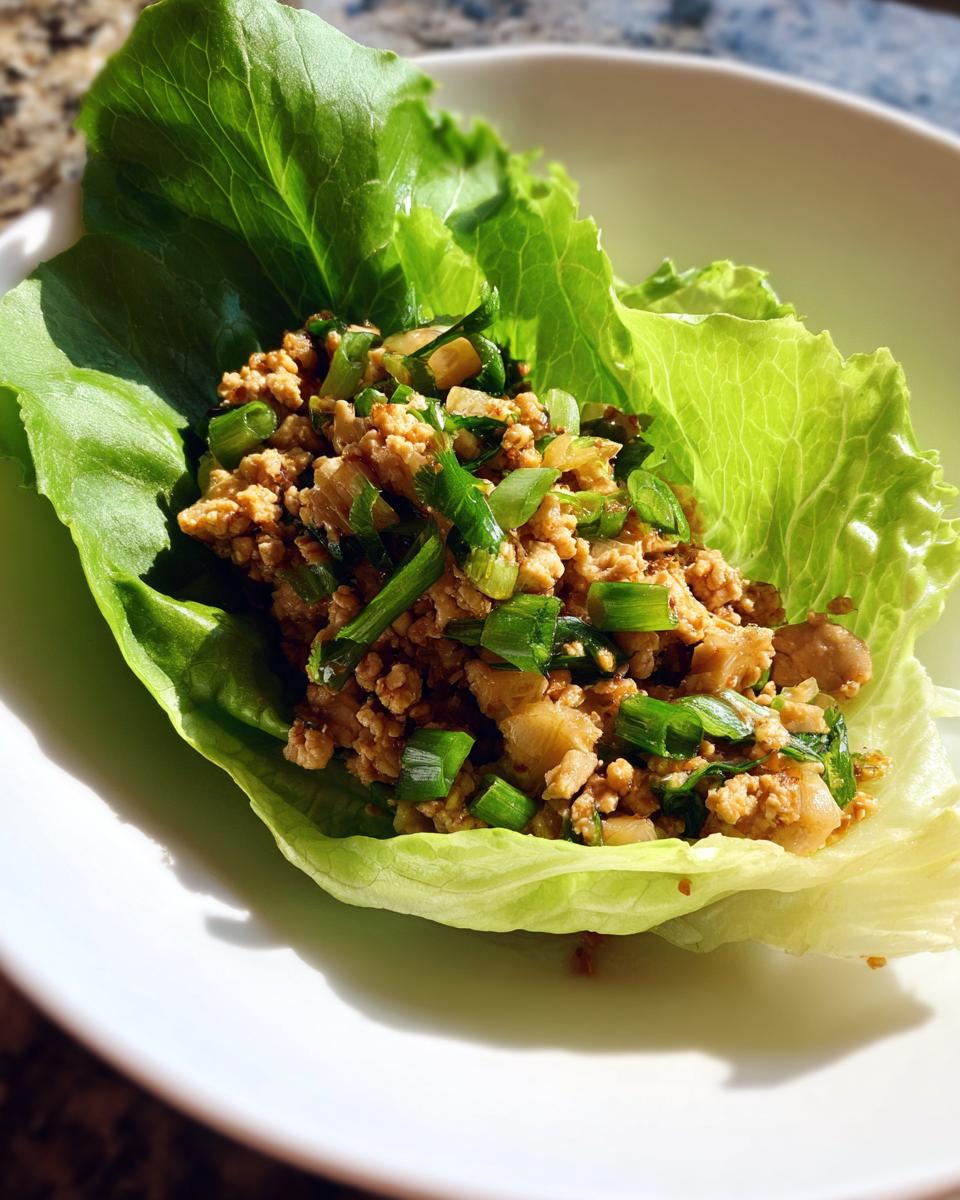 A close-up of a chicken lettuce wrap, filled with seasoned ground chicken and green onions, a perfect healthy lunch idea.