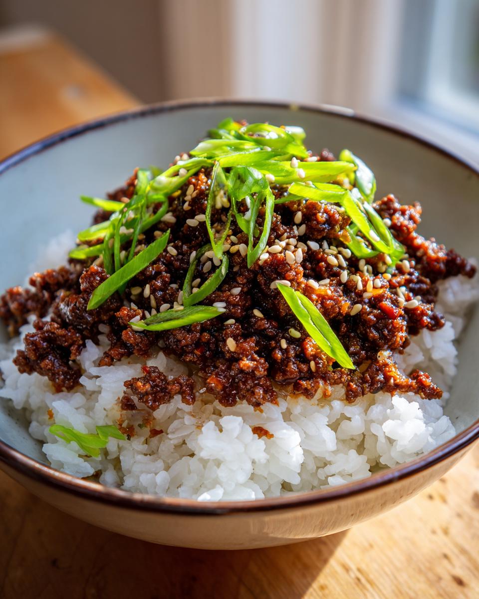 A close-up of a Korean Ground Beef Bowl, featuring seasoned ground beef over fluffy white rice, garnished with green onions and sesame seeds.