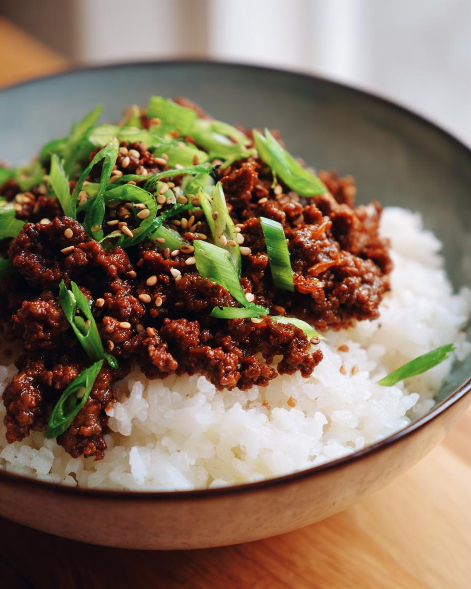 A close-up of a Korean Ground Beef Bowl, featuring seasoned ground beef over white rice, garnished with chopped green onions and sesame seeds.