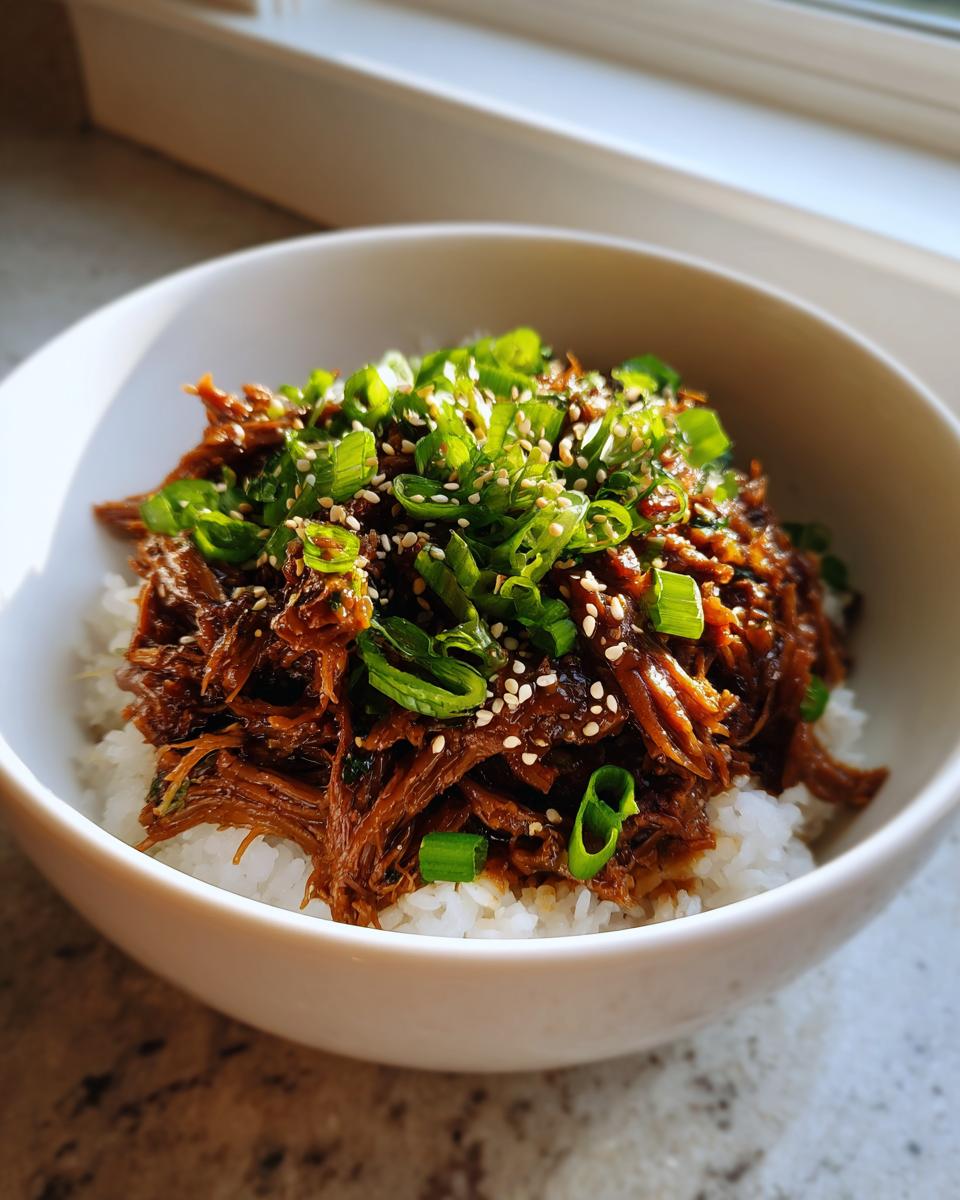 A bowl of white rice topped with tender Korean Style Pot Roast, garnished with green onions and sesame seeds.