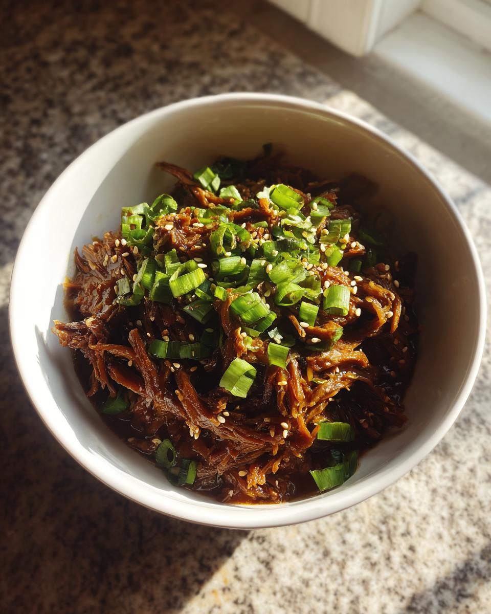 A bowl of shredded Korean Style Pot Roast topped with chopped green onions and sesame seeds.