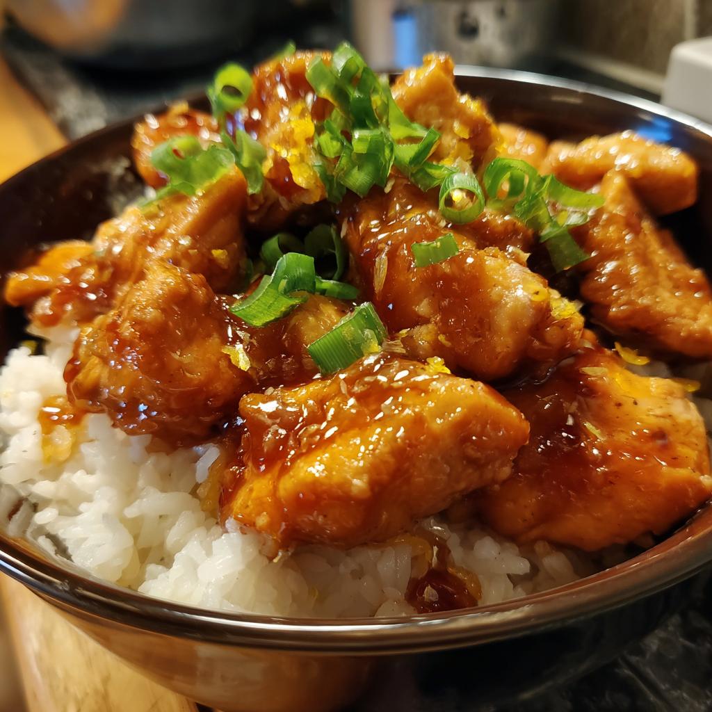A close-up of a bowl filled with fluffy white rice topped with glazed pieces of One-Pan Honey BBQ Chicken and garnished with green onions.