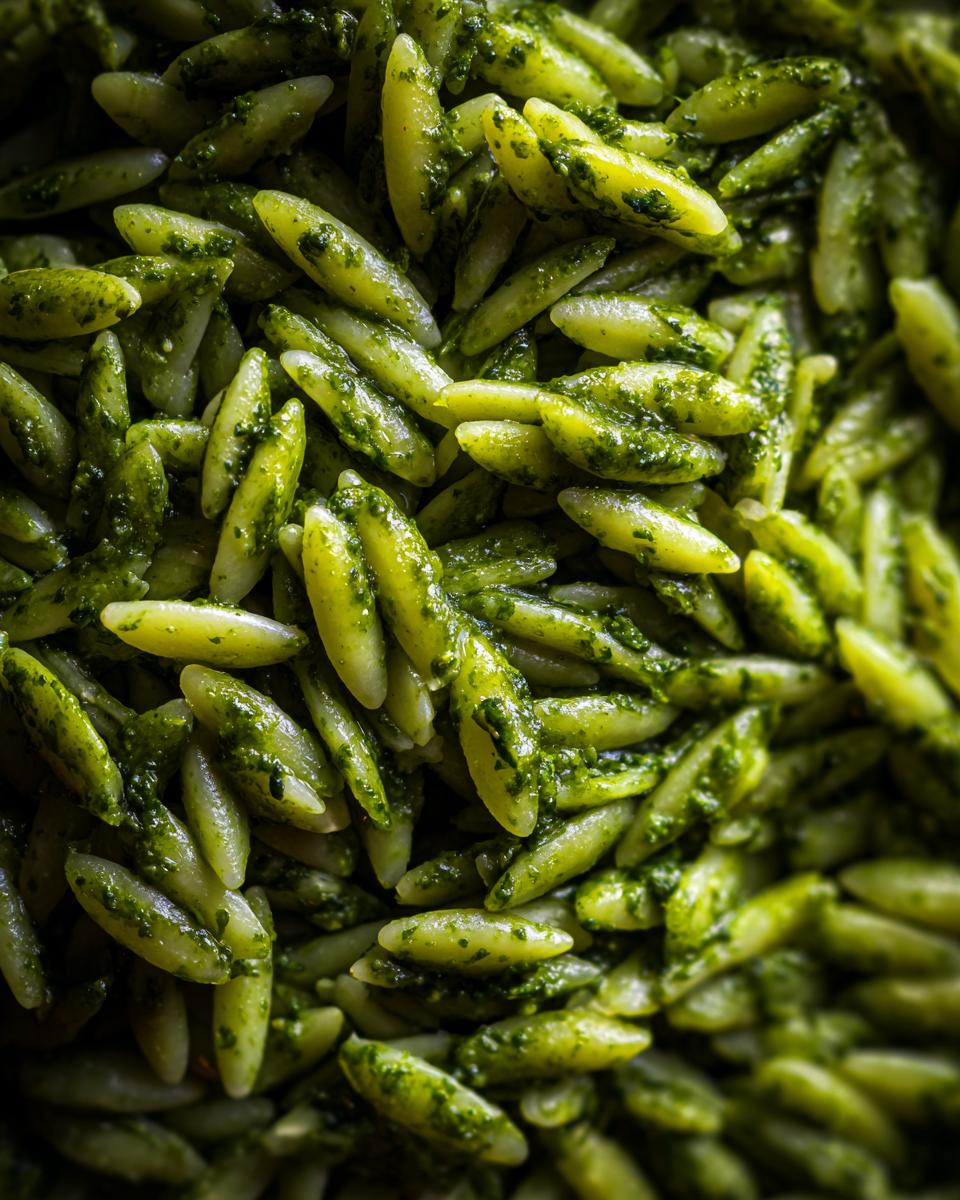 Close-up of bright green pesto orzo pasta, showcasing the vibrant sauce coating the small pasta shapes.