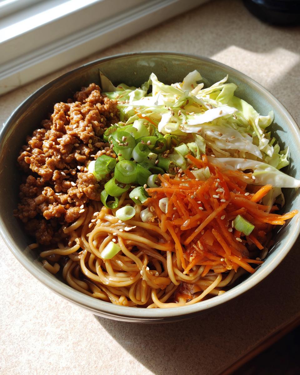 A delicious Potsticker Noodle Bowl with Pork & Cabbage Slaw, featuring noodles, ground pork, shredded carrots, cabbage, and green onions.