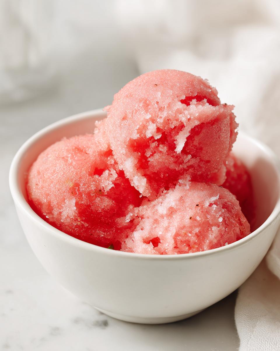 A white bowl filled with scoops of refreshing watermelon sorbet, showcasing its pink hue and icy texture.